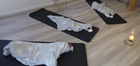 Drei Sportmatten mit je einer Decke und einem Polaroid Bild darauf, liegen in einem Raum vor einer Kerze.